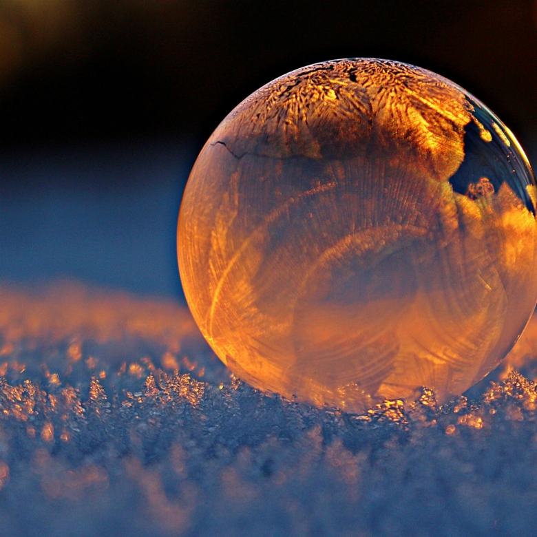Close-up shot of a frozen bubble with warm reflections resting on a snowy surface at twilight.